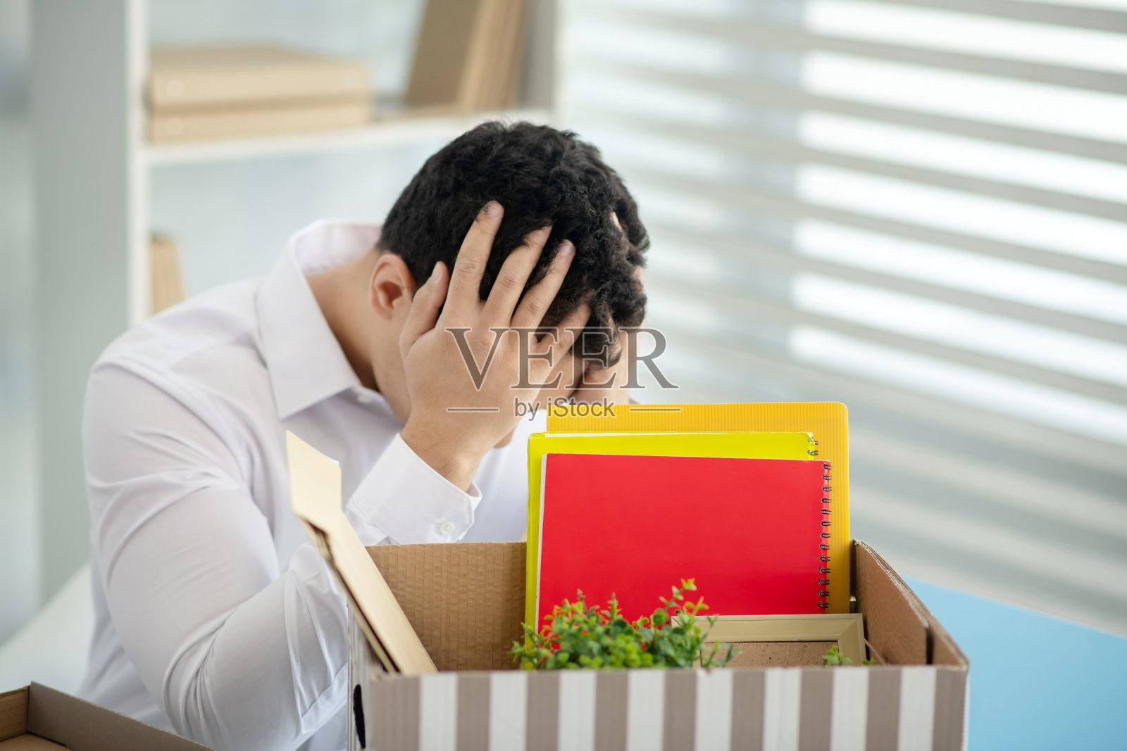 沮丧的黑发男子坐在桌旁,双手抱头照片摄影图片