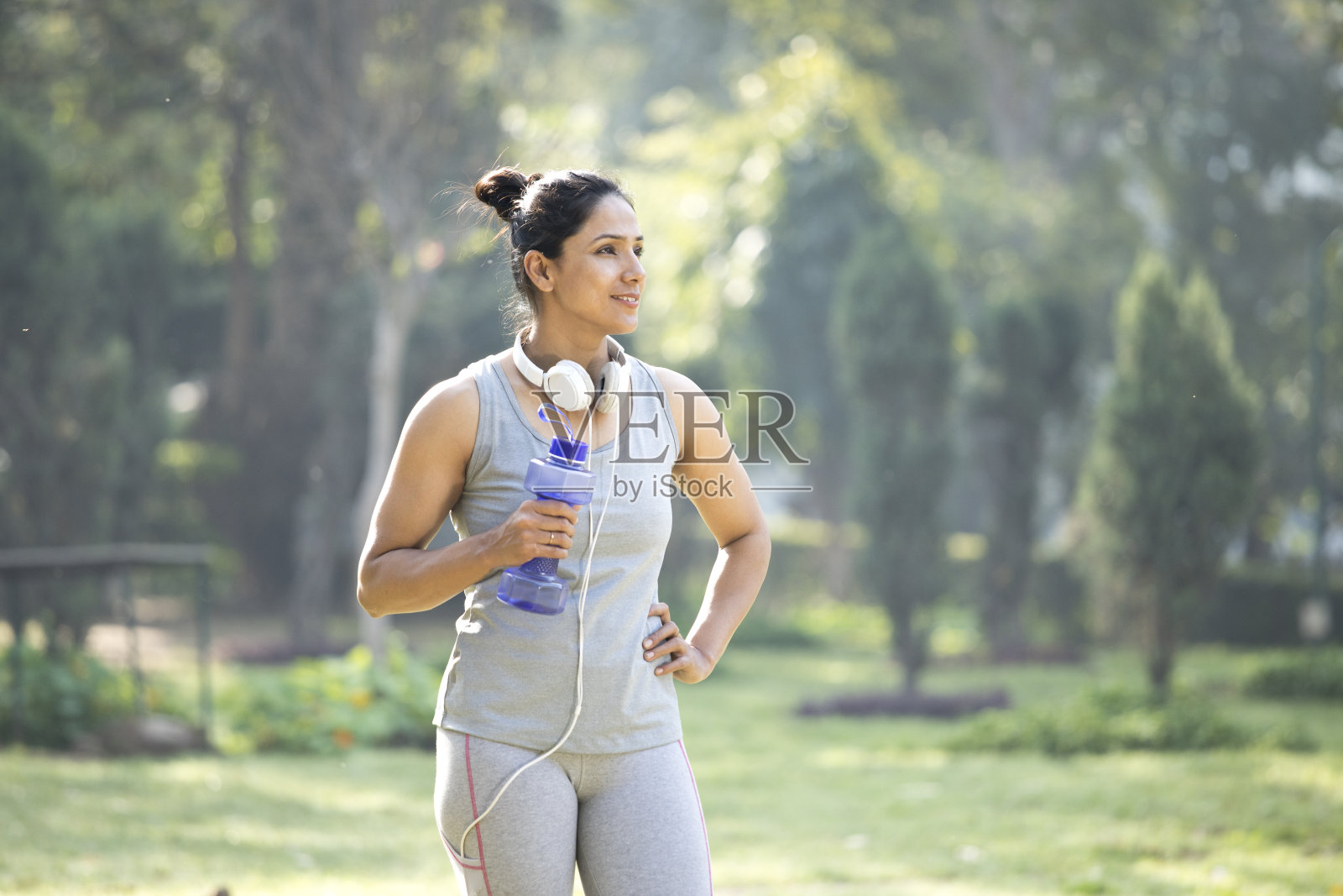 在公园里戴着哑铃形状的水瓶和耳机的健康女性照片摄影图片