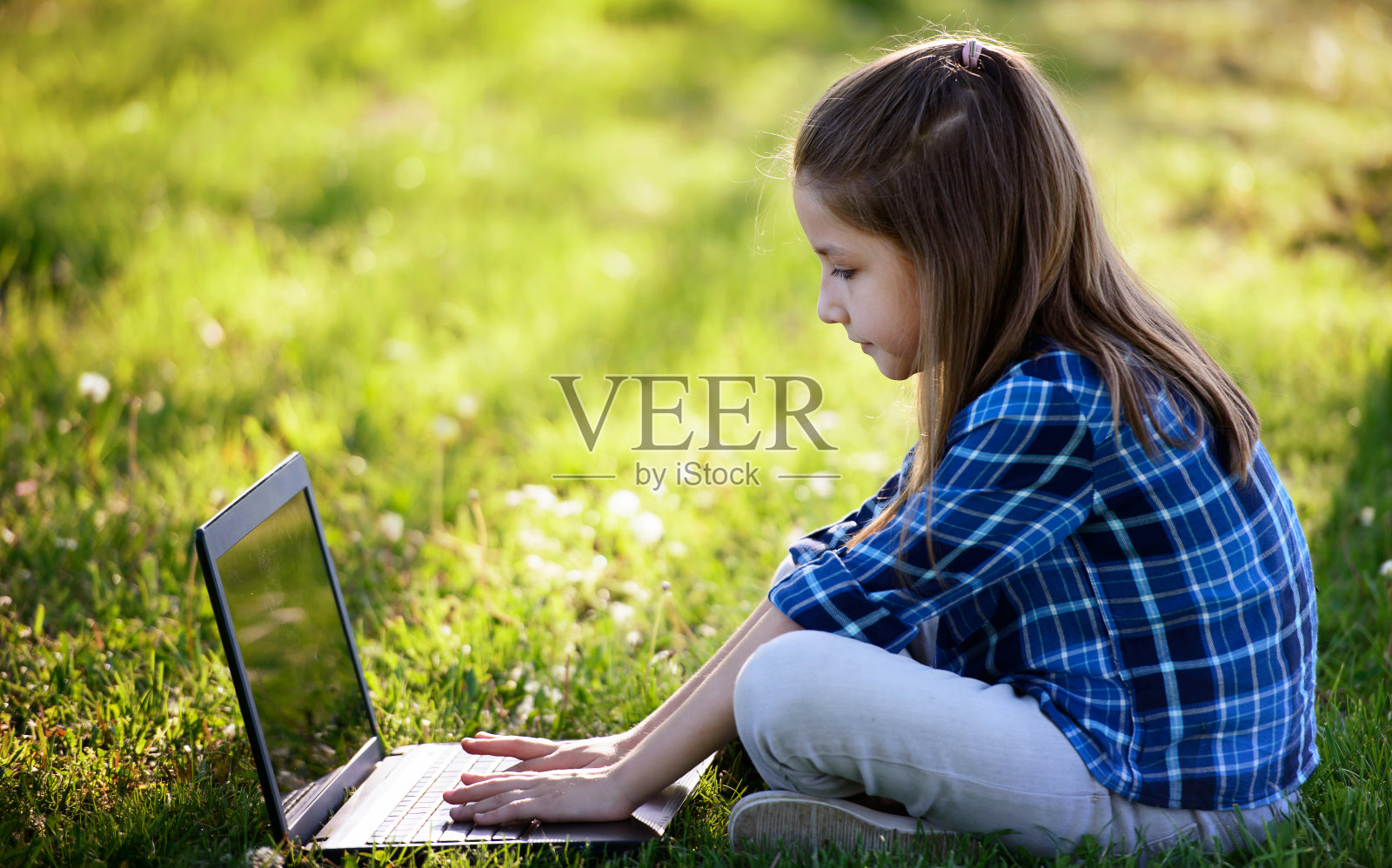 小女孩坐在草地上玩笔记本电脑。教育、生活方式、科技理念照片摄影图片