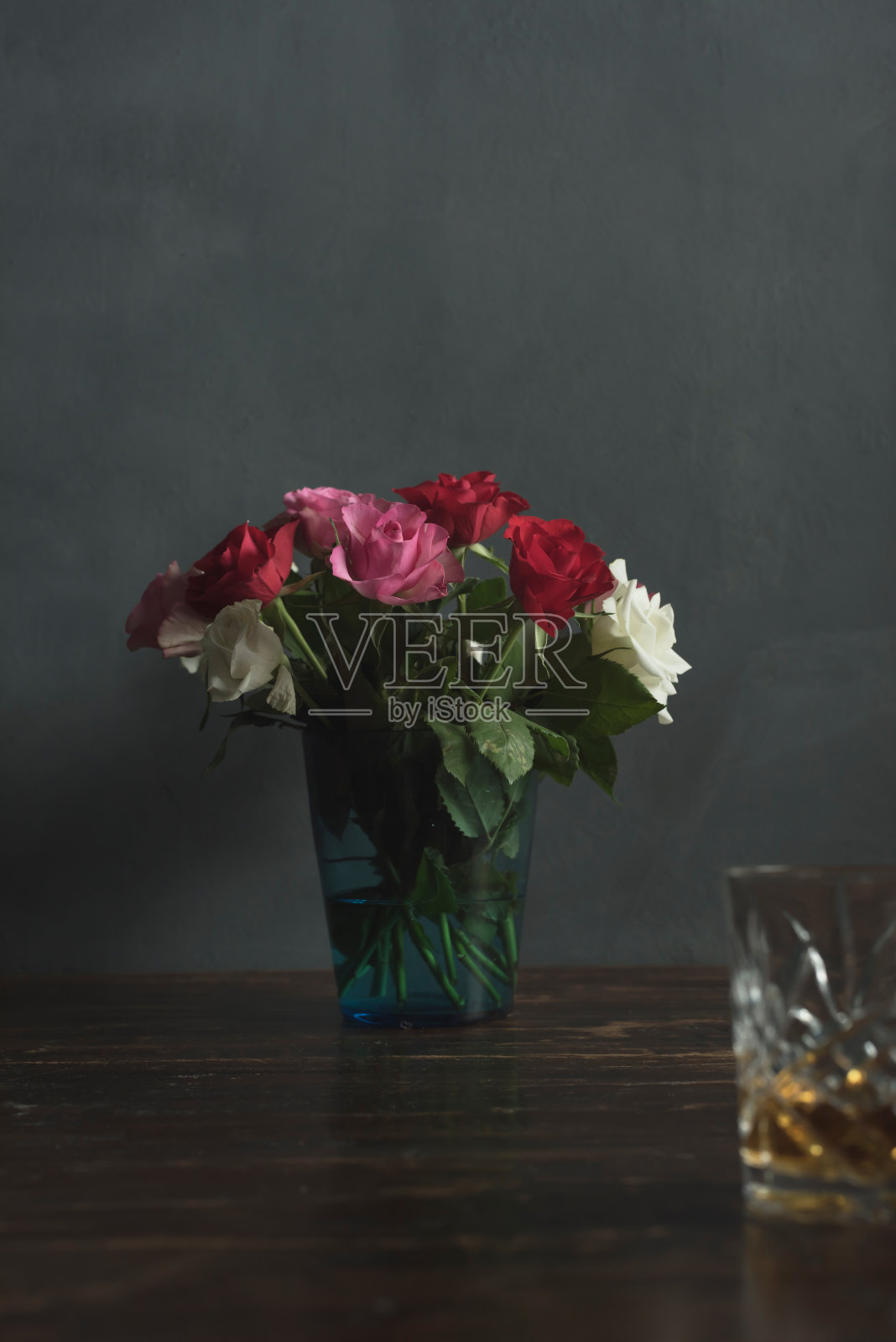 木桌上的玫瑰花瓶和威士忌酒杯照片摄影图片