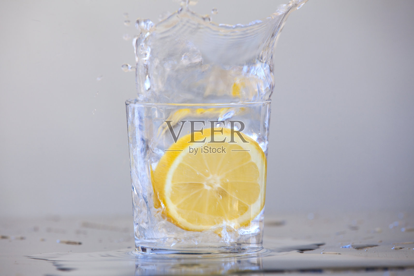 柠檬滴在一杯水中。柠檬水照片摄影图片