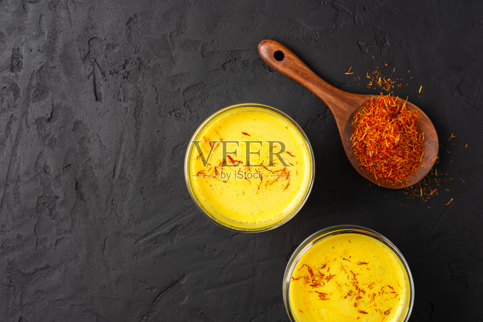 藏红花拿铁在一个玻璃杯里,在黑色的混凝土背景,木勺干香料藏红花,金色牛奶,俯视图,复制空间照片摄影图片