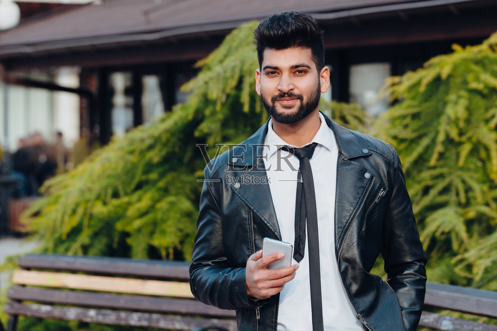 一名留着胡子的印度男子在街上使用智能手机上的应用程序。照片摄影图片