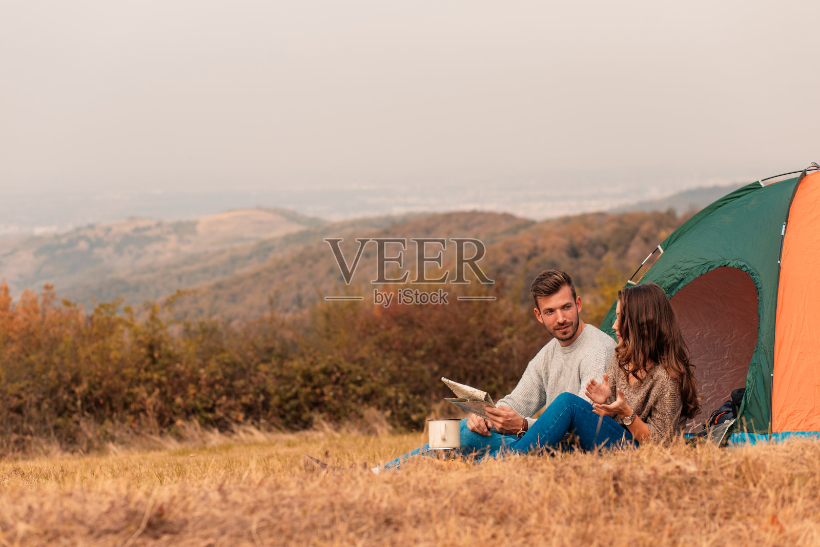 快乐的年轻夫妇坐在帐篷露营花时间在一起。照片摄影图片