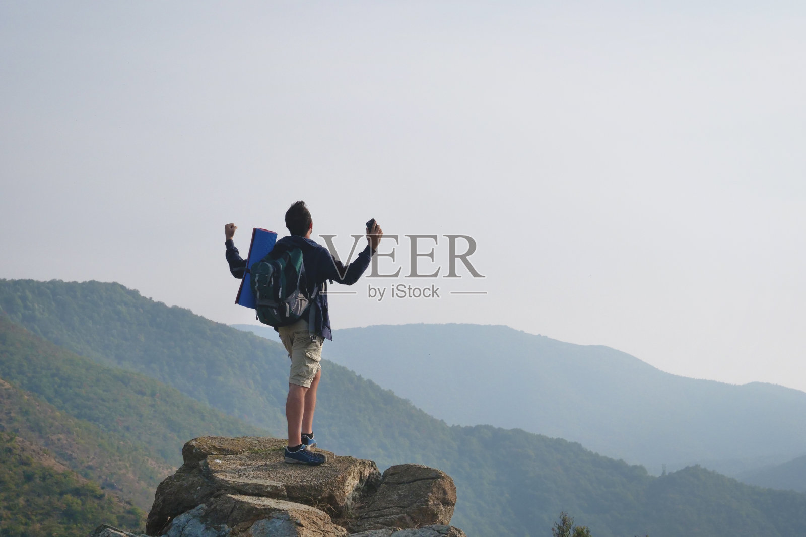 在一个岩石峭壁的边缘,一个男人向天空举起双手,表示自由或胜利,背景是一幅奇异的风景。照片摄影图片