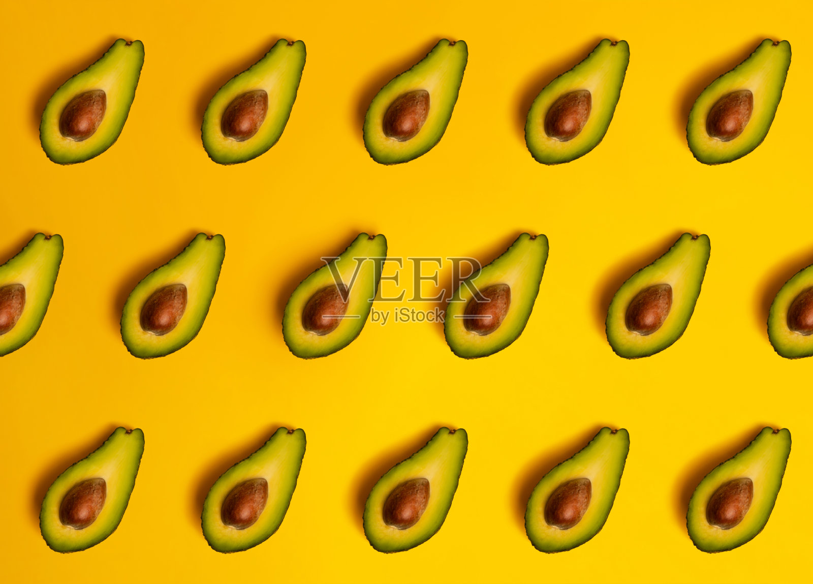 熟透的、多汁的、对半切开的鳄梨配上黄色的固体底色。照片摄影图片