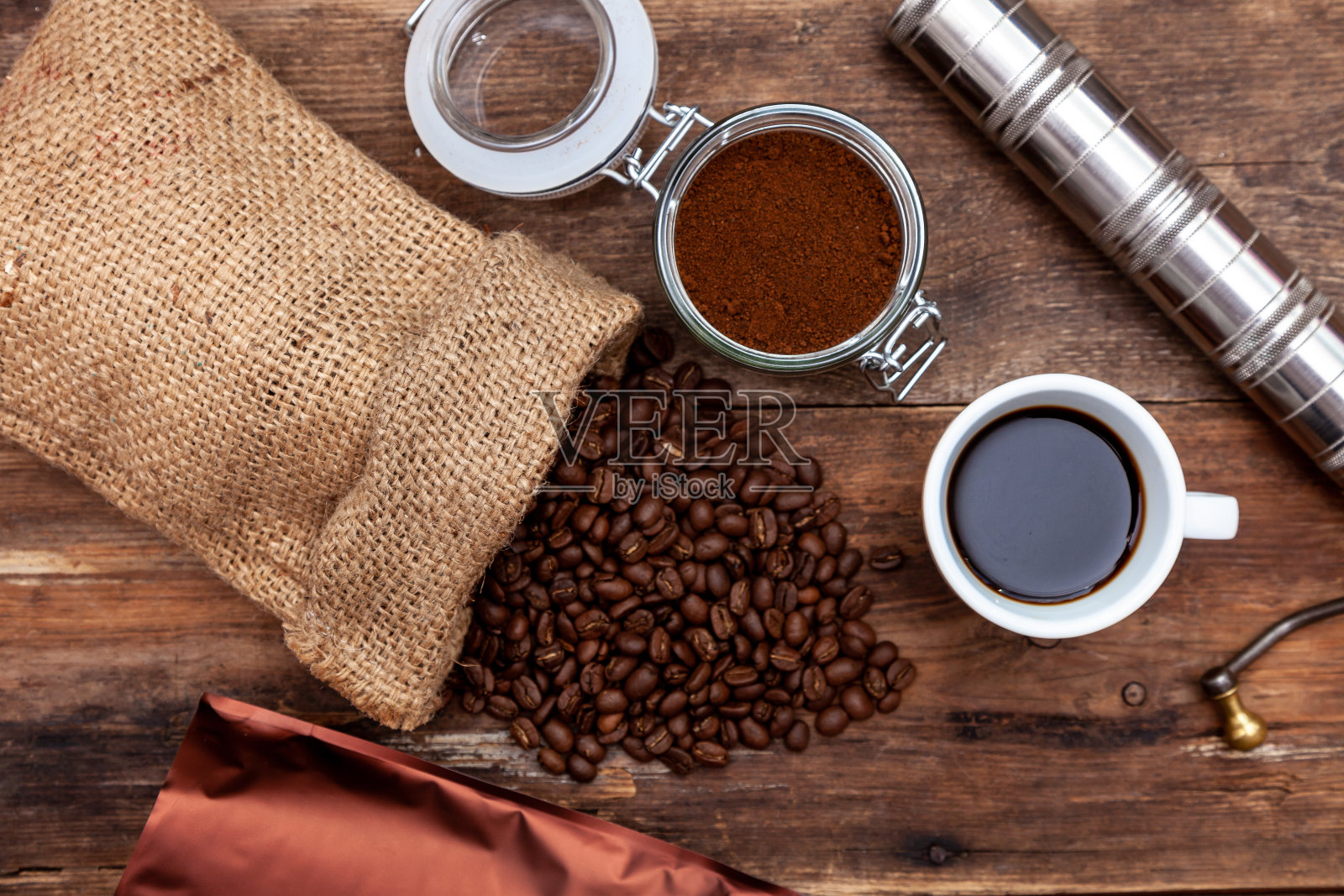 木桌上有一袋咖啡。在罐子里磨碎的咖啡豆。手动咖啡研磨机。俯视图,放置文本。棕色的背景。把咖啡装在包里。喝一杯就能变白照片摄影图片