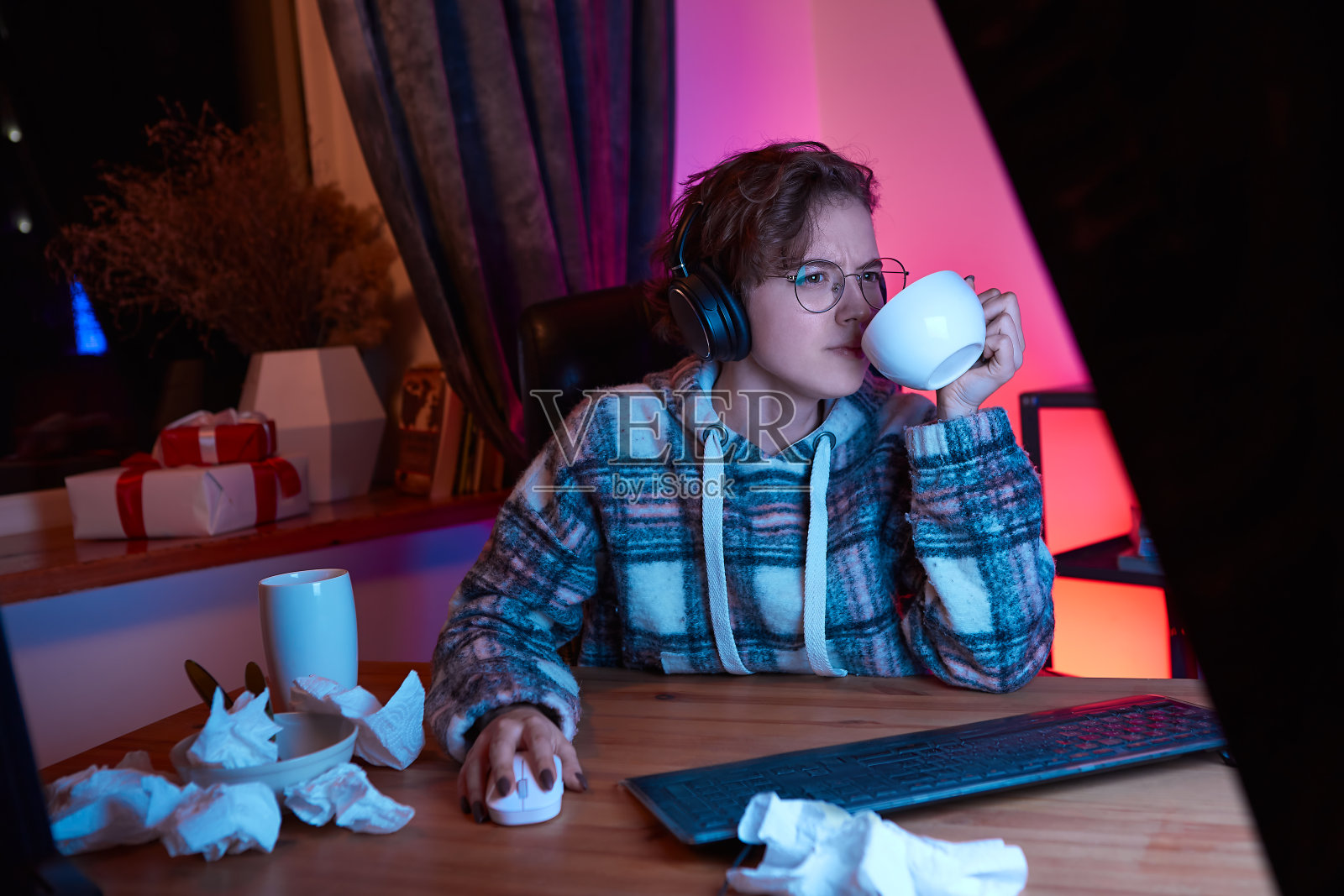 年轻女子一边在电脑上看视频,一边用杯子喝咖啡。国内检疫照片摄影图片