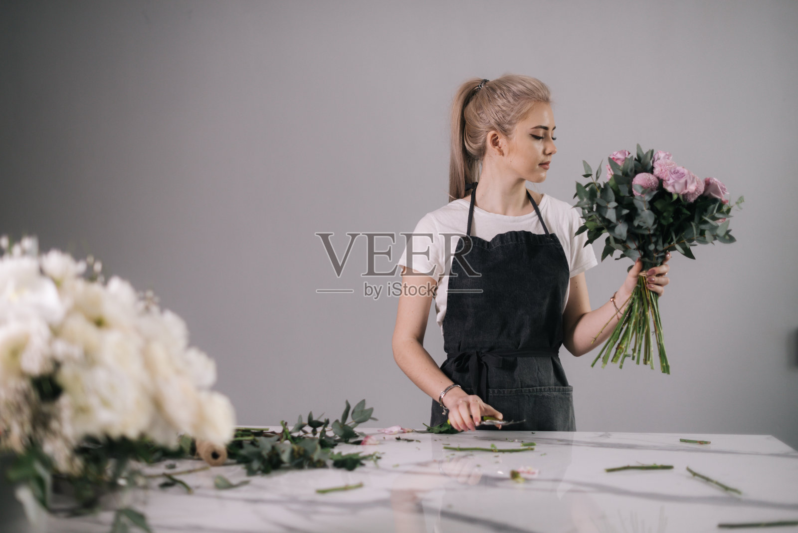 年轻漂亮的卖花女,系着围裙,拿着一束花站在桌子旁照片摄影图片