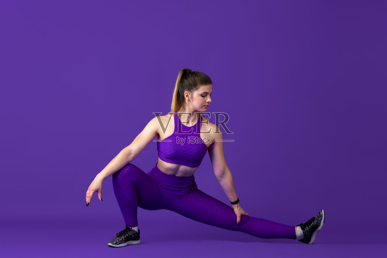 美丽的年轻女运动员练习在紫色的工作室背景,单色肖像照片摄影图片