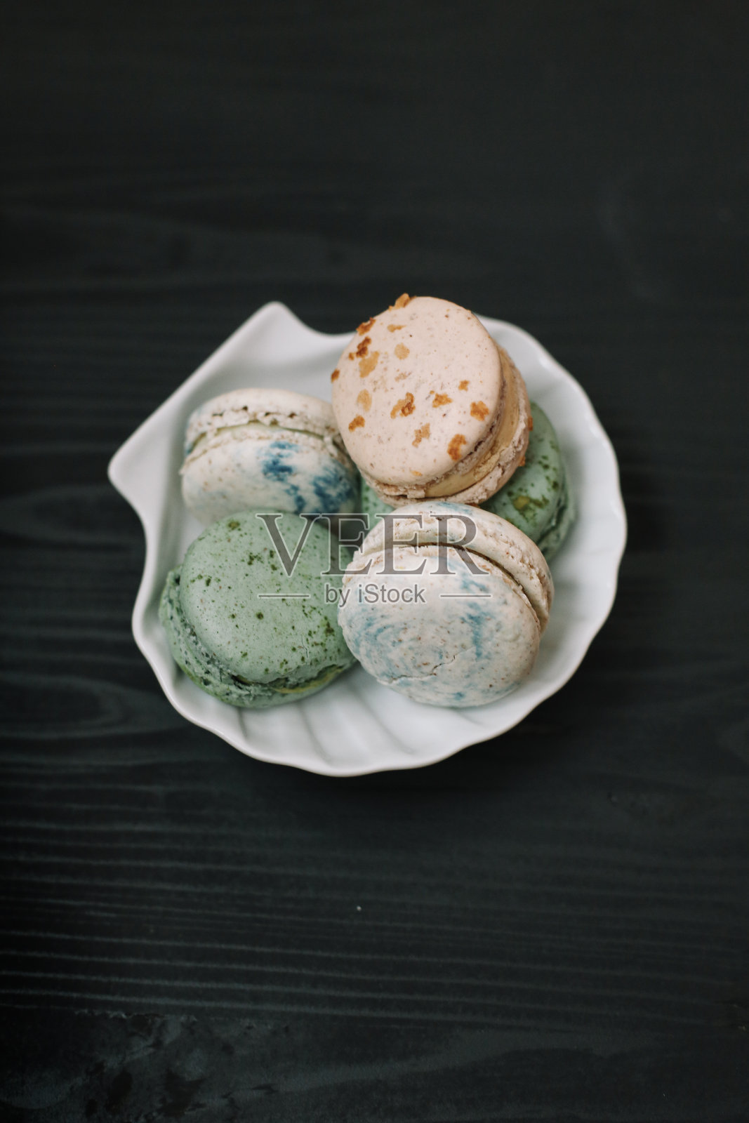 彩色的自制马卡龙躺在白色的盘子上,黑色的木制背景。模式。照片摄影图片