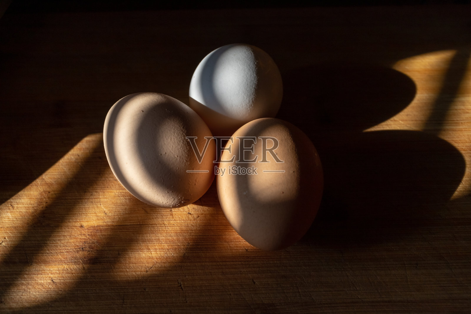 新鲜的鸡蛋躺在一块木板上,美丽温暖的灯光温暖地照射着它照片摄影图片