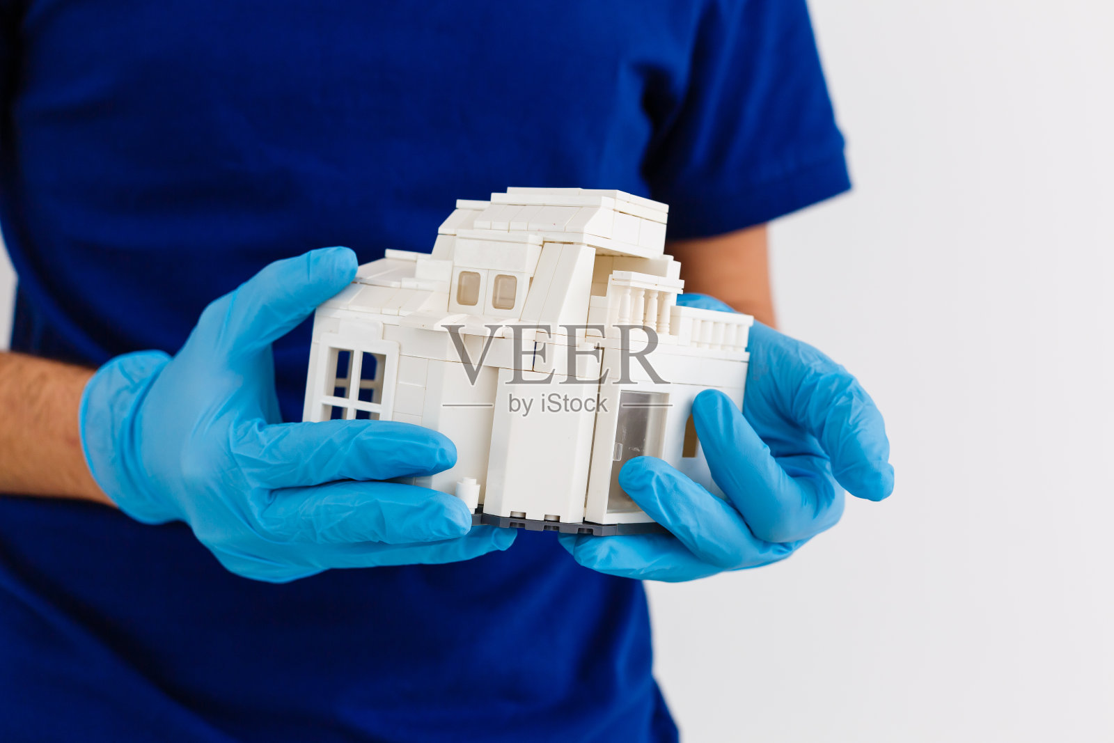 手掌中的小木屋配有白色医用橡胶手套,蓝色背景,木屋的木制模型,检疫概念,冠状病毒大流行,疫情期间的药物照片摄影图片