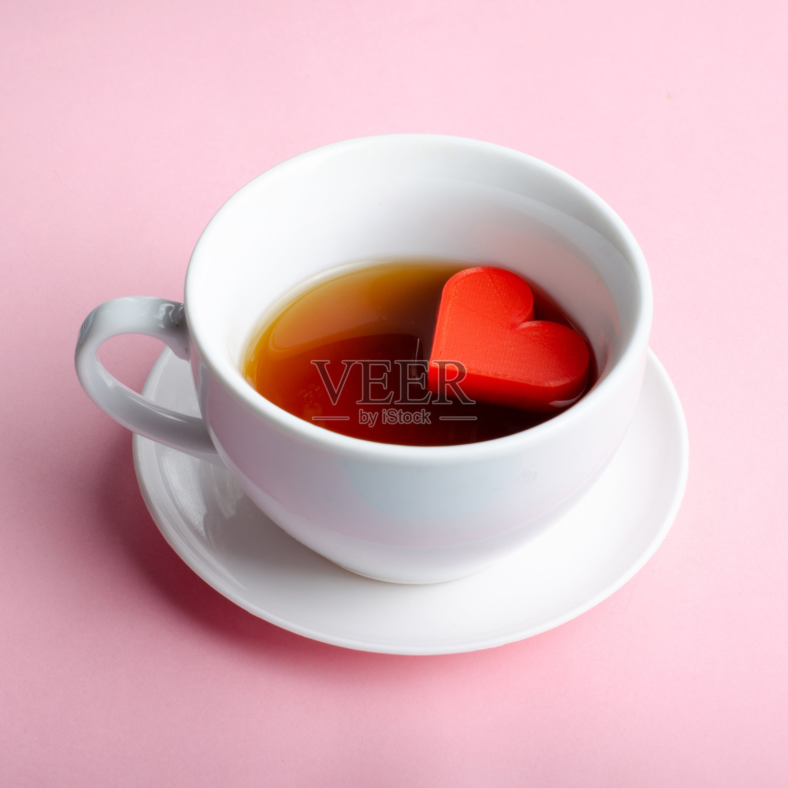 一杯白色的茶或咖啡,粉红色的背景上有一个心形的小雕像。爱情的概念约会,浪漫,友谊和没有人的对象之间的关系照片摄影图片