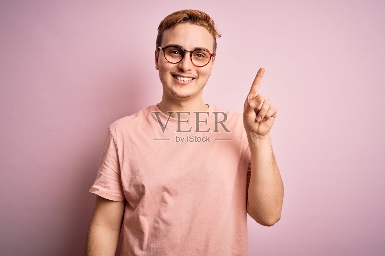 年轻英俊的红发男子穿着休闲t恤站在孤立的粉红色背景指向成功的想法。退出和快乐。第一。照片摄影图片