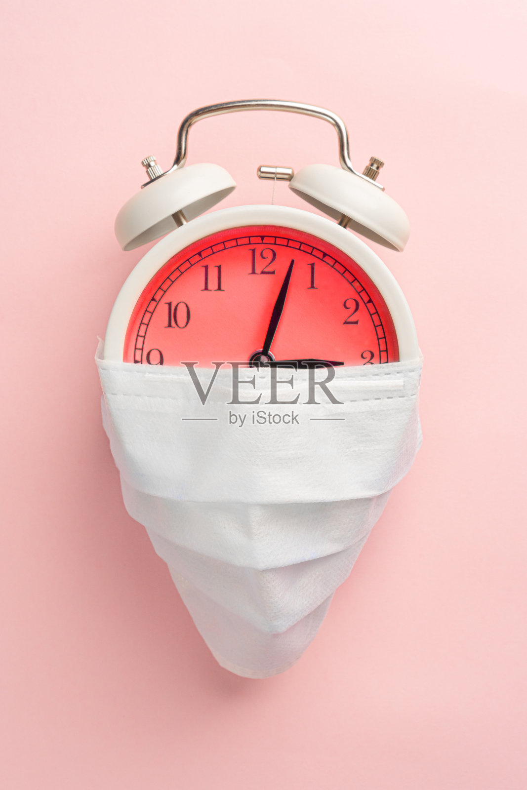 医用一次性口罩上有一个红色表盘的闹钟。在粉红色的背景上照片摄影图片