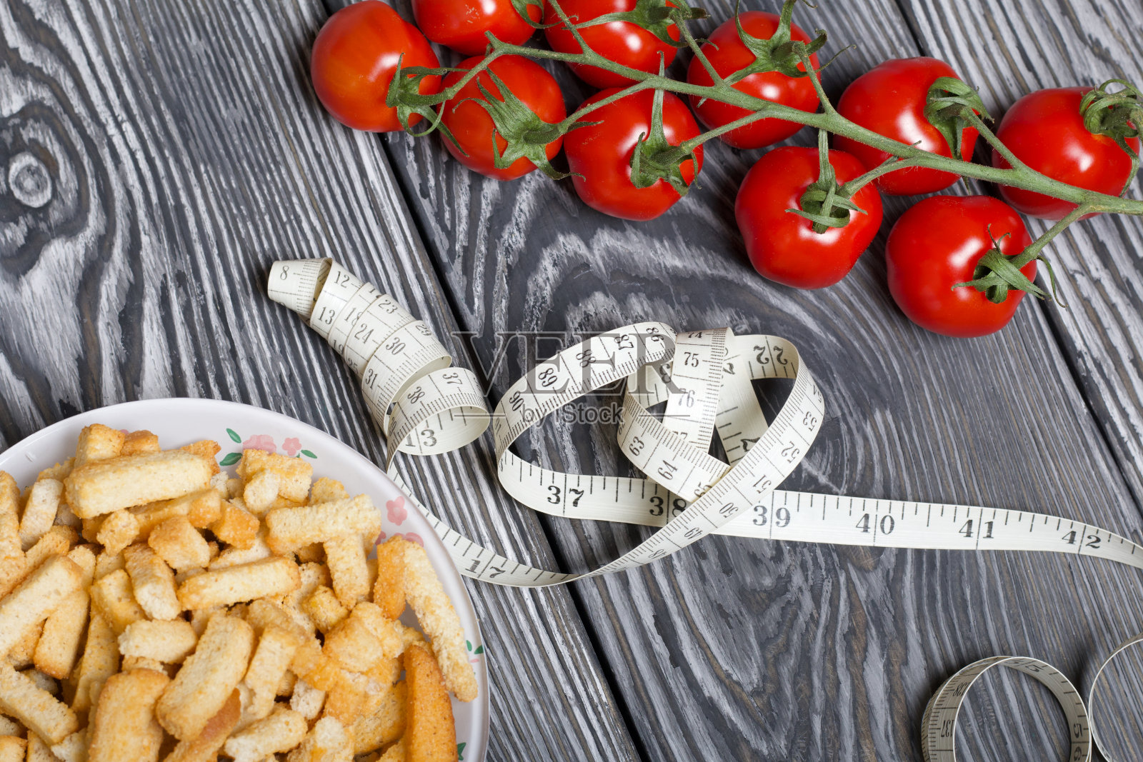 几串西红柿和一杯饼干。他们之间有一根卷尺。在刷过的松木板上。世界无饮食日标志。照片摄影图片
