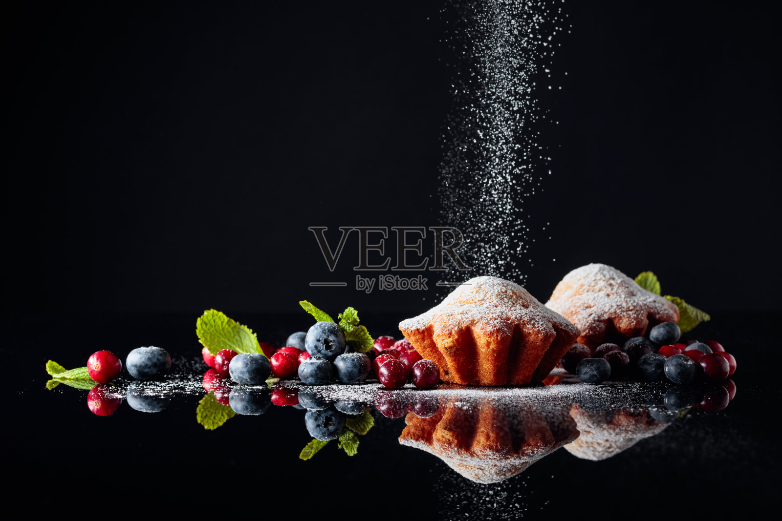 蔓越莓和蓝莓松饼撒上糖粉在黑色反光的背景上。浆果和薄荷松饼。照片摄影图片
