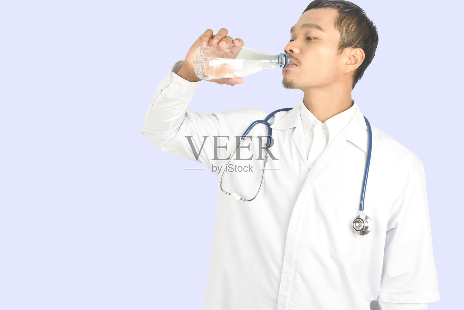 年轻的男子医生与听诊器站着,并持有目前的饮用水为健康在淡蓝色的背景。照片摄影图片