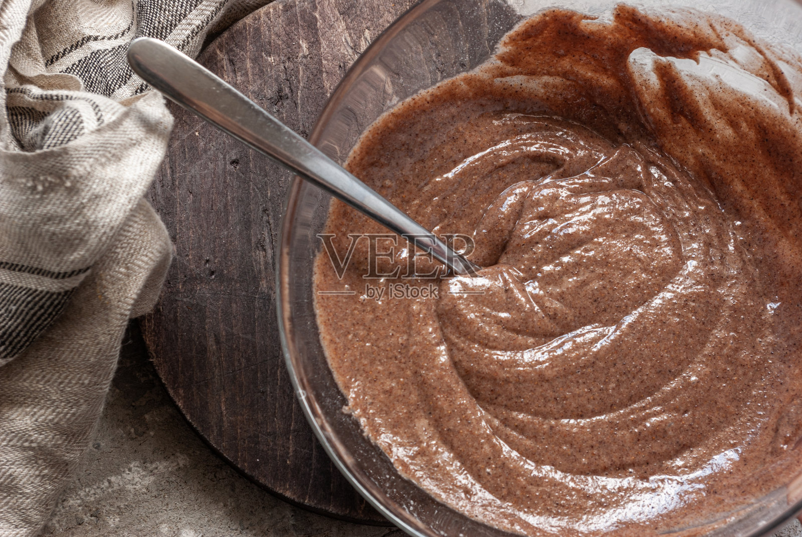 放在玻璃碗里做海龟蛋糕的面团。在一张灰色混凝土桌子上的一块深色木板上,旁边放着一条米色的毛巾。烘焙烹饪过程。照片摄影图片