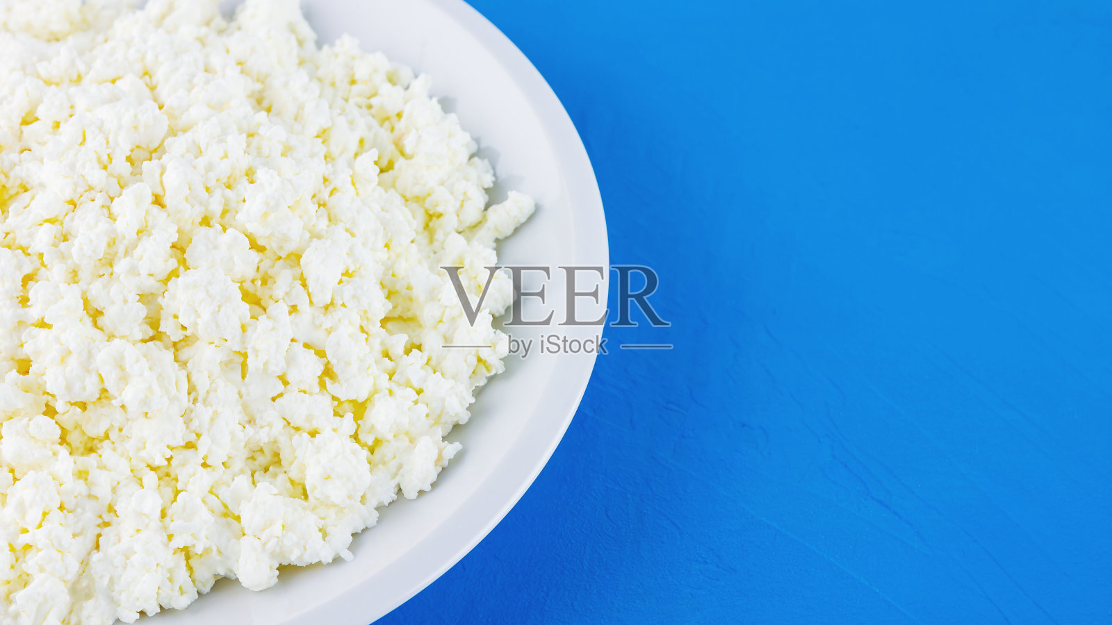 蓝底白盘子里的白软干酪。有机生态健康餐、乳制品。一盘自制的干酪。前视图。本空间照片摄影图片