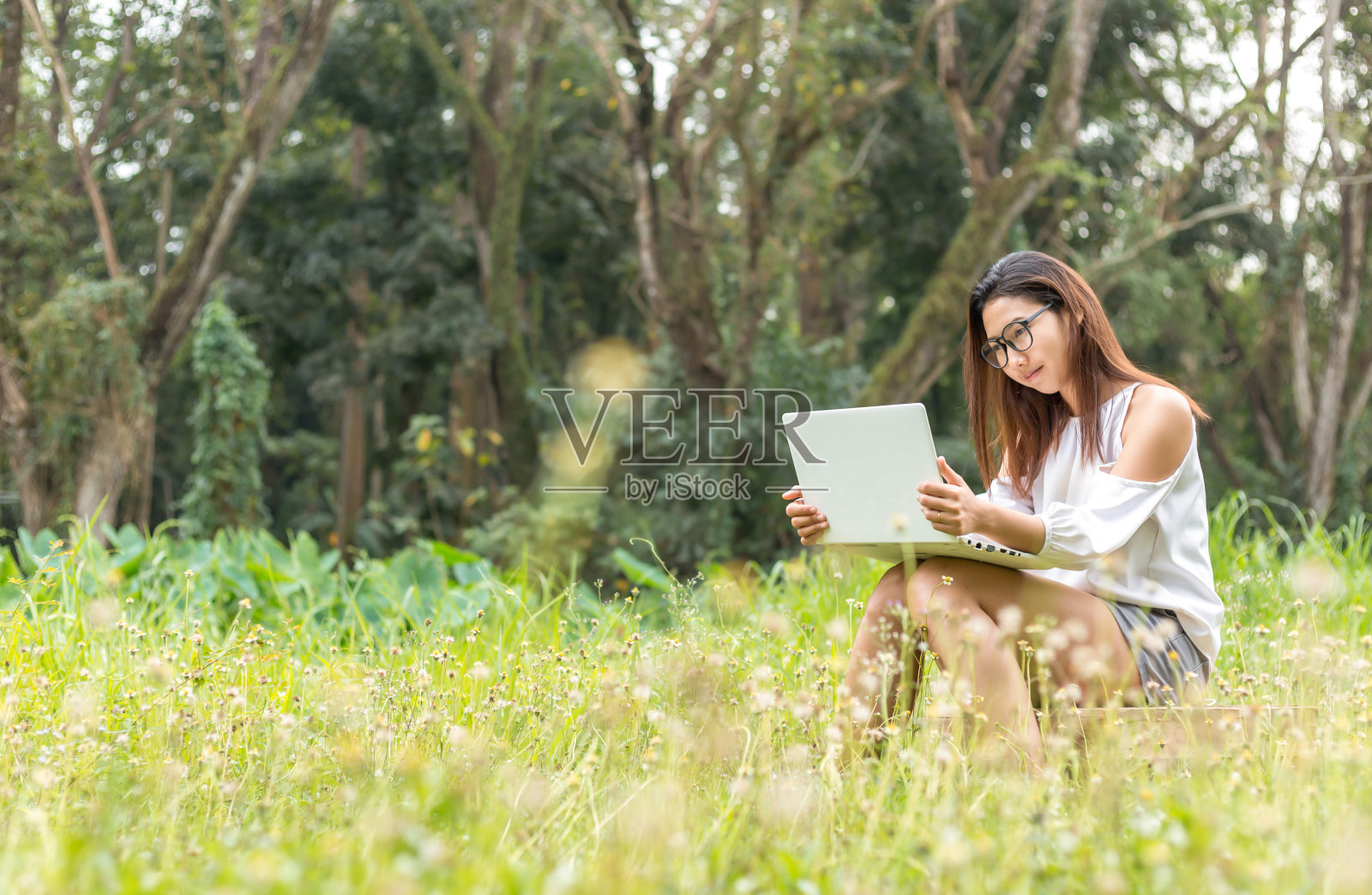 女人们坐在木箱上,用笔记本工作。她在公园里工作,颜色是橙色和绿色。照片摄影图片