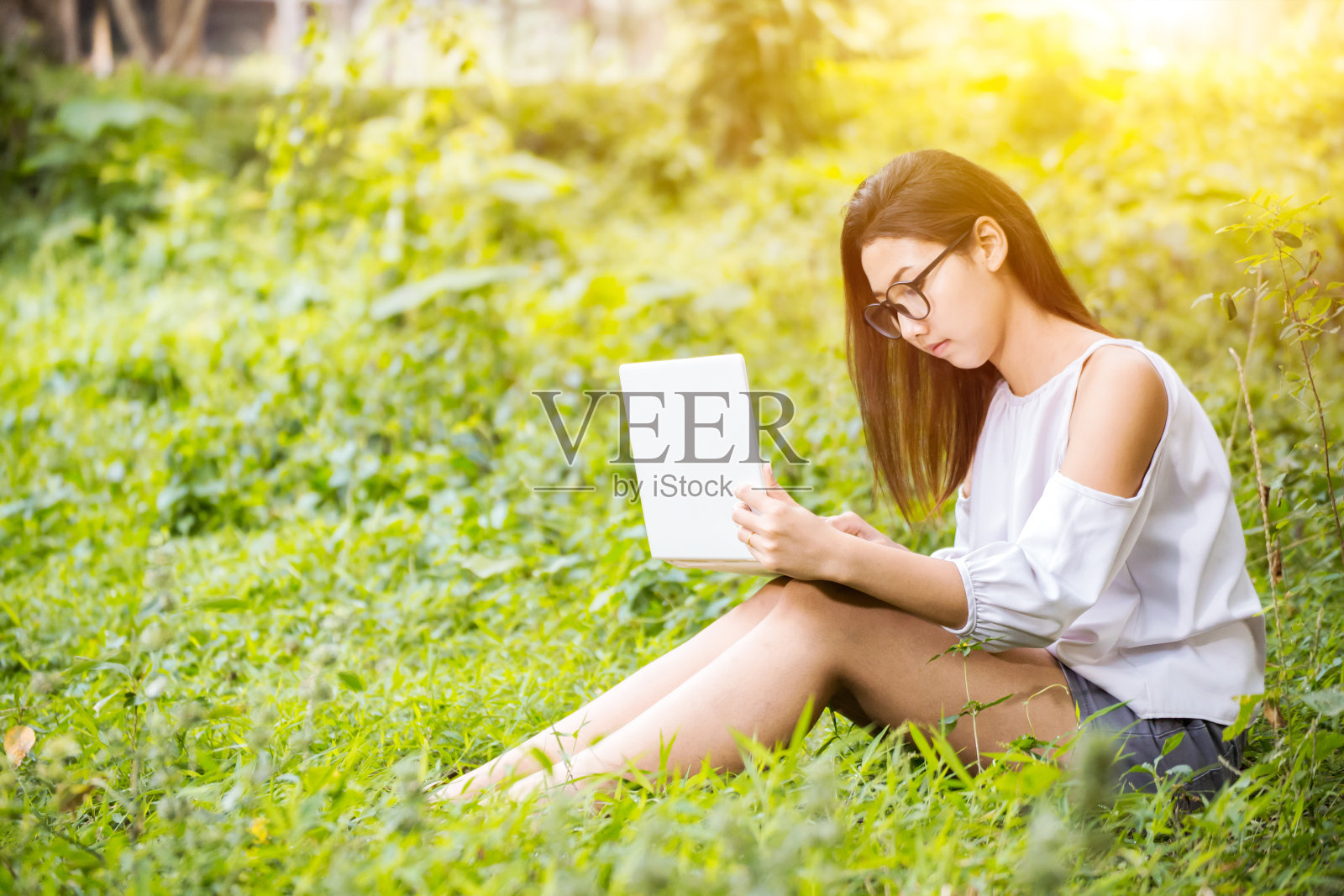 女人们坐在木箱上,用笔记本工作。她在公园里工作,颜色是橙色和绿色。照片摄影图片