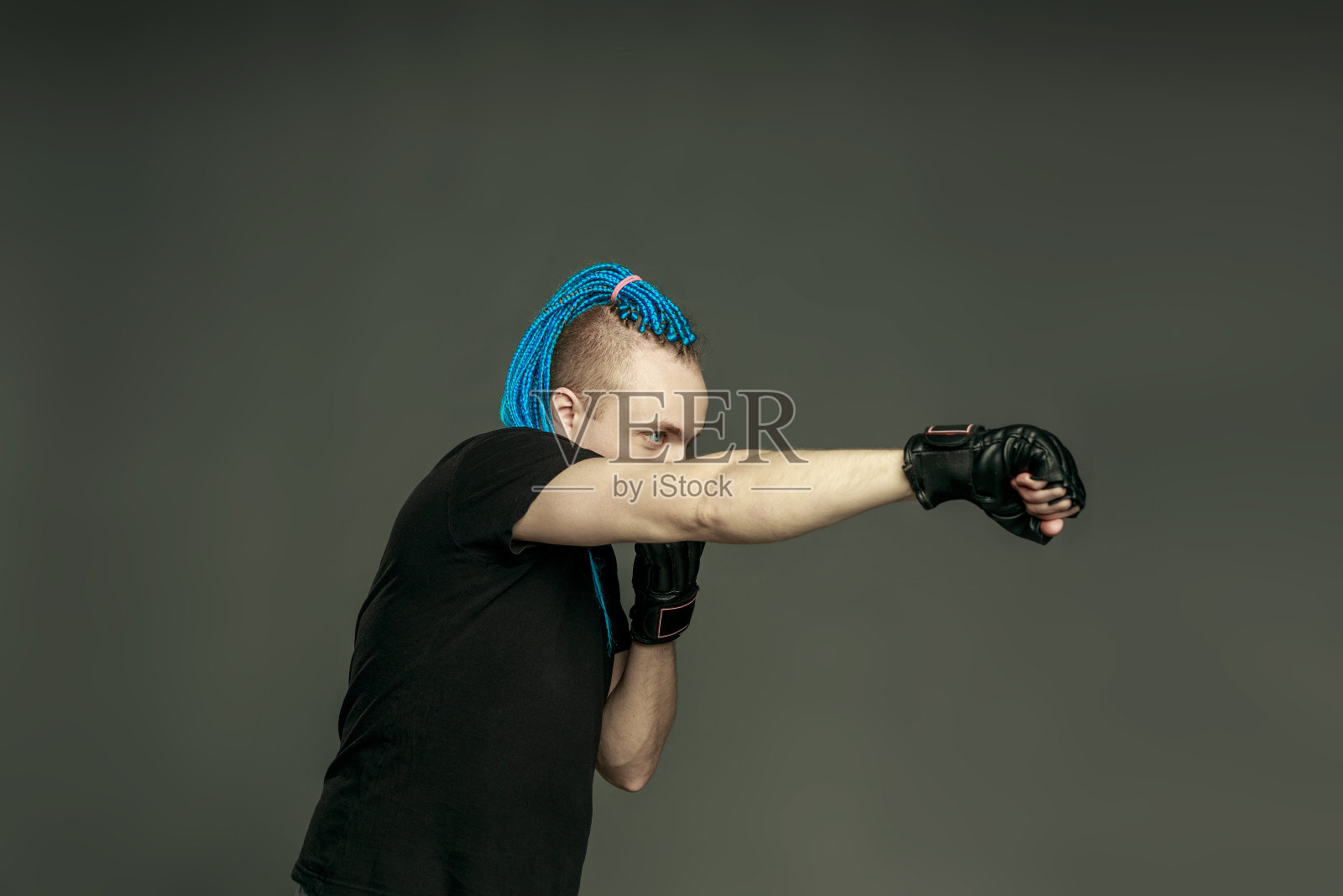 一名留着蓝色辫子的莫霍克发型的男子戴着拳击手套,准备在黑暗的背景下战斗。照片摄影图片