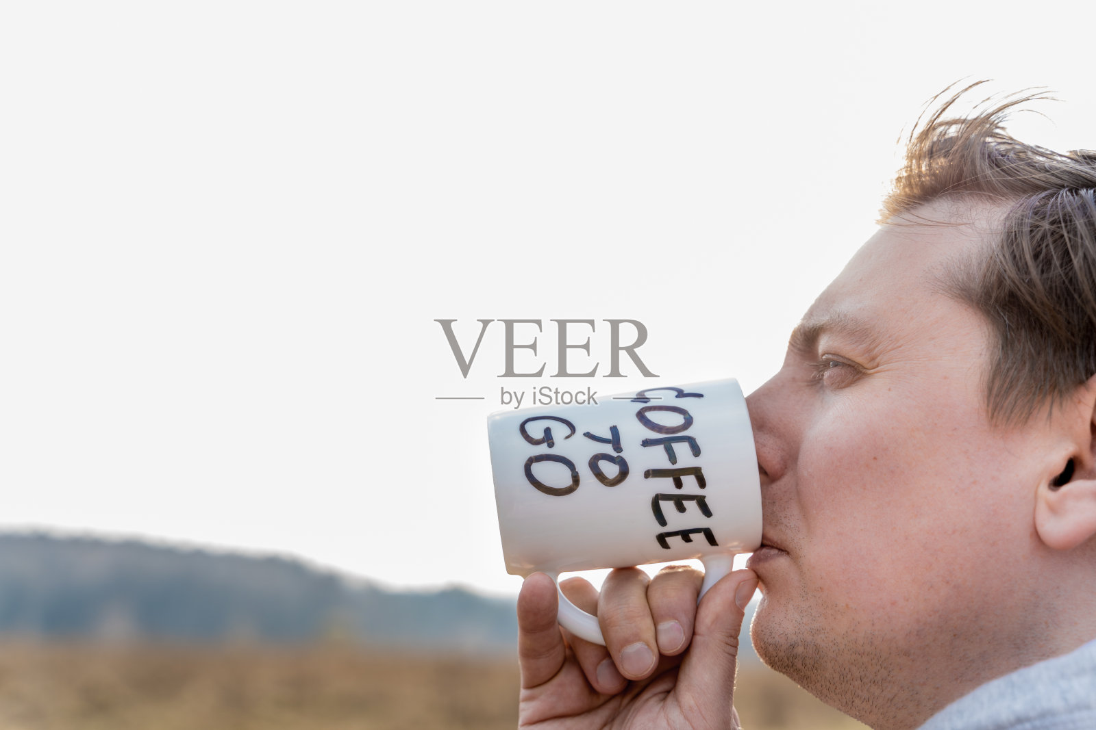 从家庭住宿累了,穿着帽衫的男人喝咖啡从白色马克杯在野外。杯子上的创意铭文标记。结束隔离,自我隔离,逃离城市。Covid-19,冠状病毒照片摄影图片