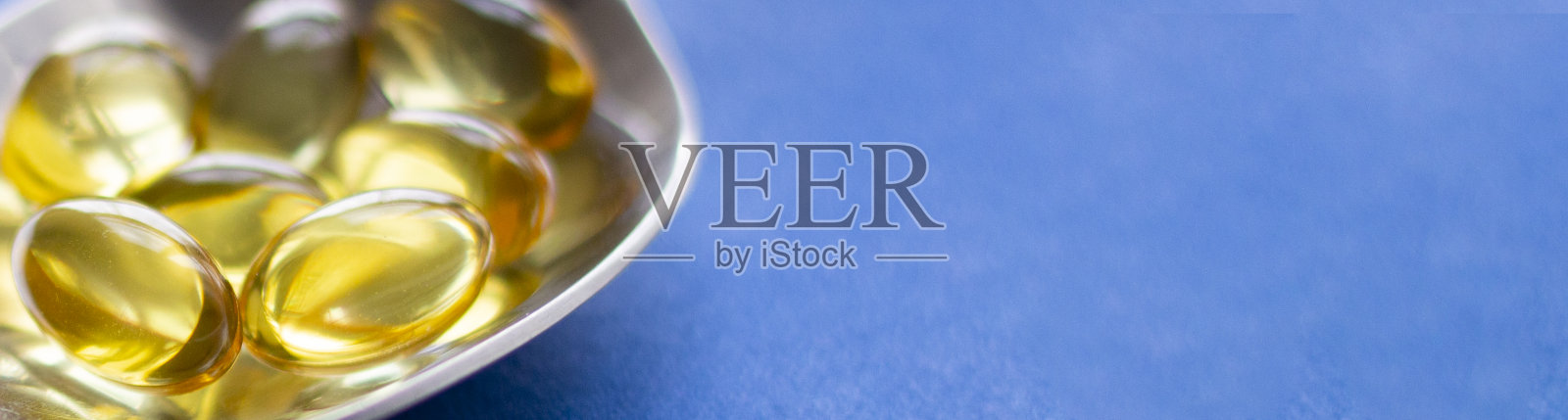 汤匙鱼油丸,蓝色背景照片摄影图片