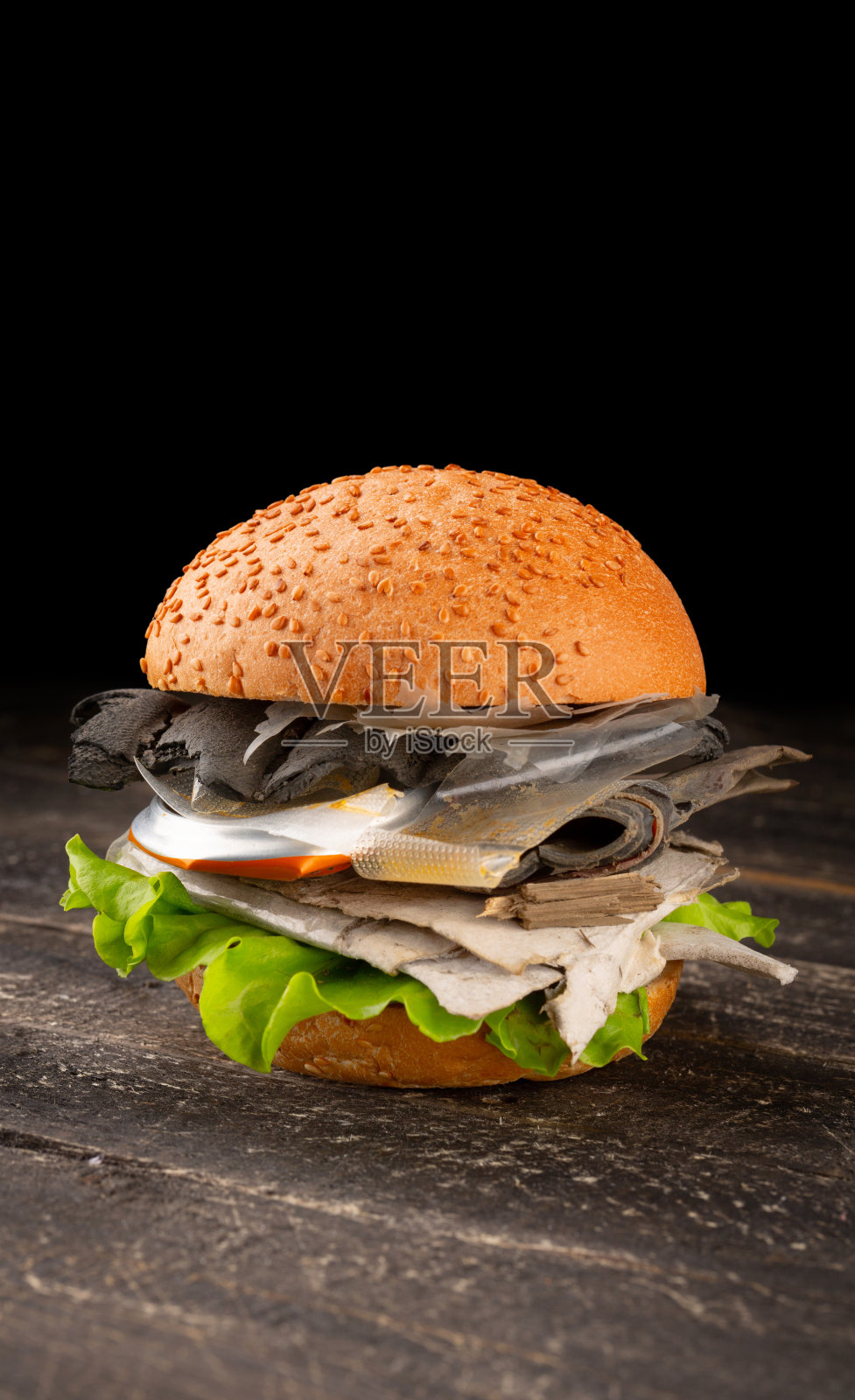 新鲜美味的汉堡,里面有塑料垃圾,背景是深色的木头。塑料污染照片摄影图片