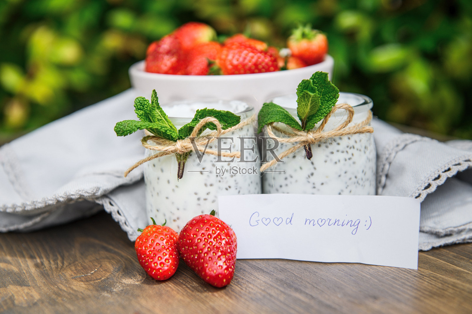 木桌上放着两杯天然酸奶,上面点缀着薄荷和草莓。照片摄影图片