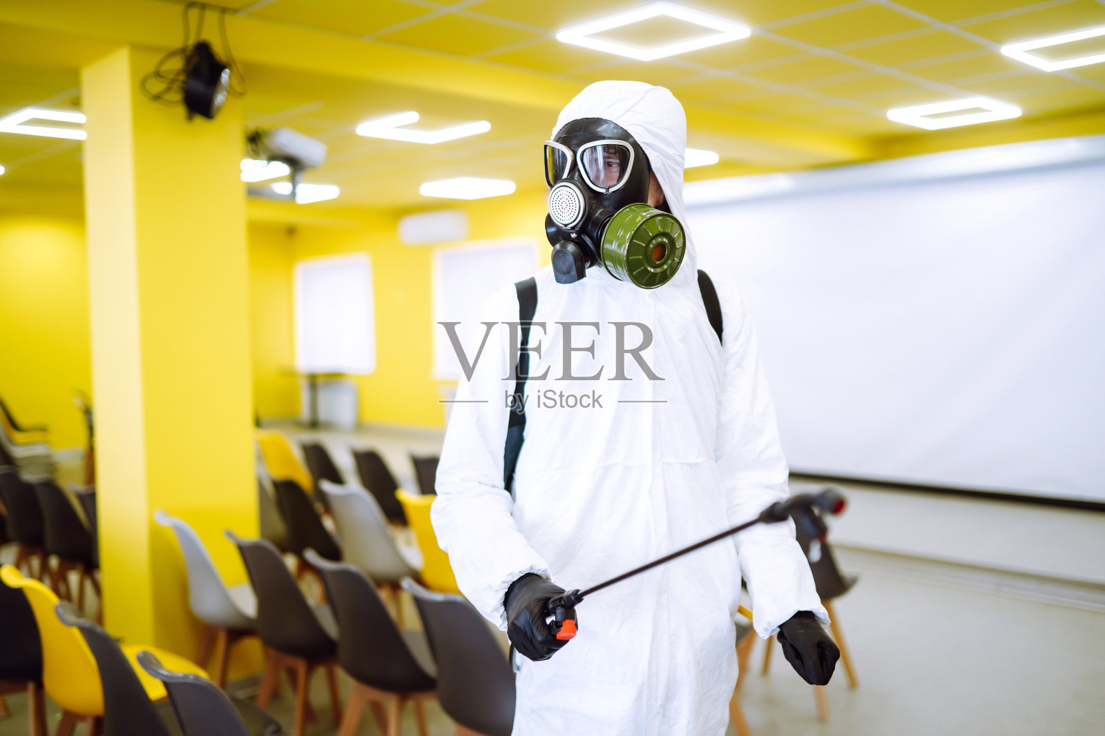 穿着防护服的人正在礼堂消毒。照片摄影图片