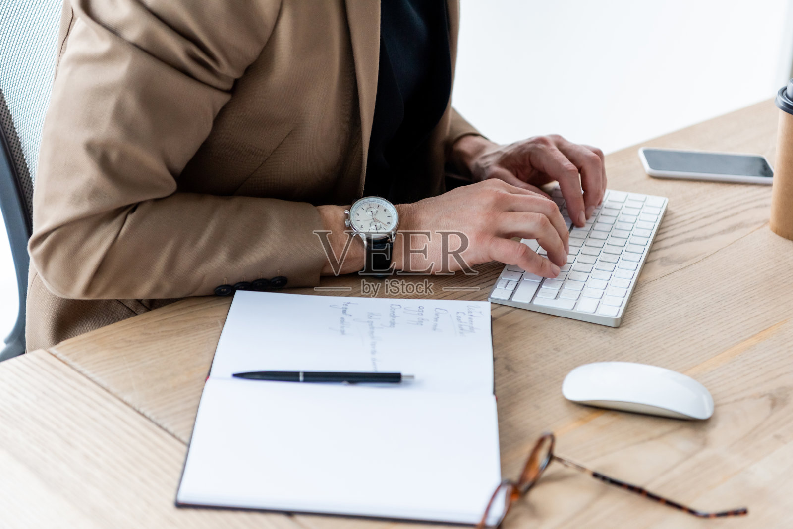 商业人士在笔记本、笔、电脑鼠标和智能手机附近的空白屏幕上敲击电脑键盘照片摄影图片