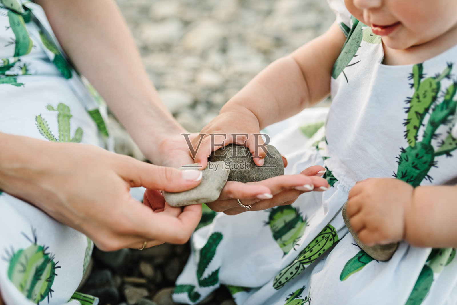 妈妈和女儿坐在湖边的沙滩上玩石头。暑假的概念。母亲的,宝宝的一天。花时间在一起。家人看。照片摄影图片