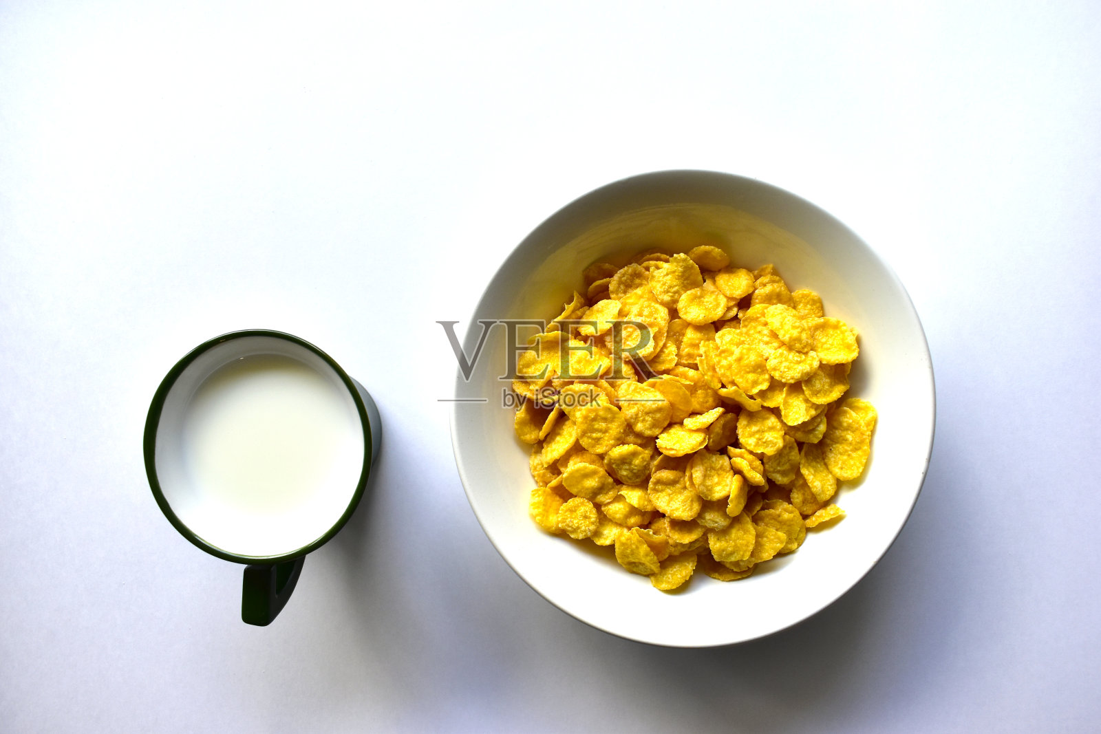 一杯牛奶里的黄色玉米片,背景是白色。照片摄影图片
