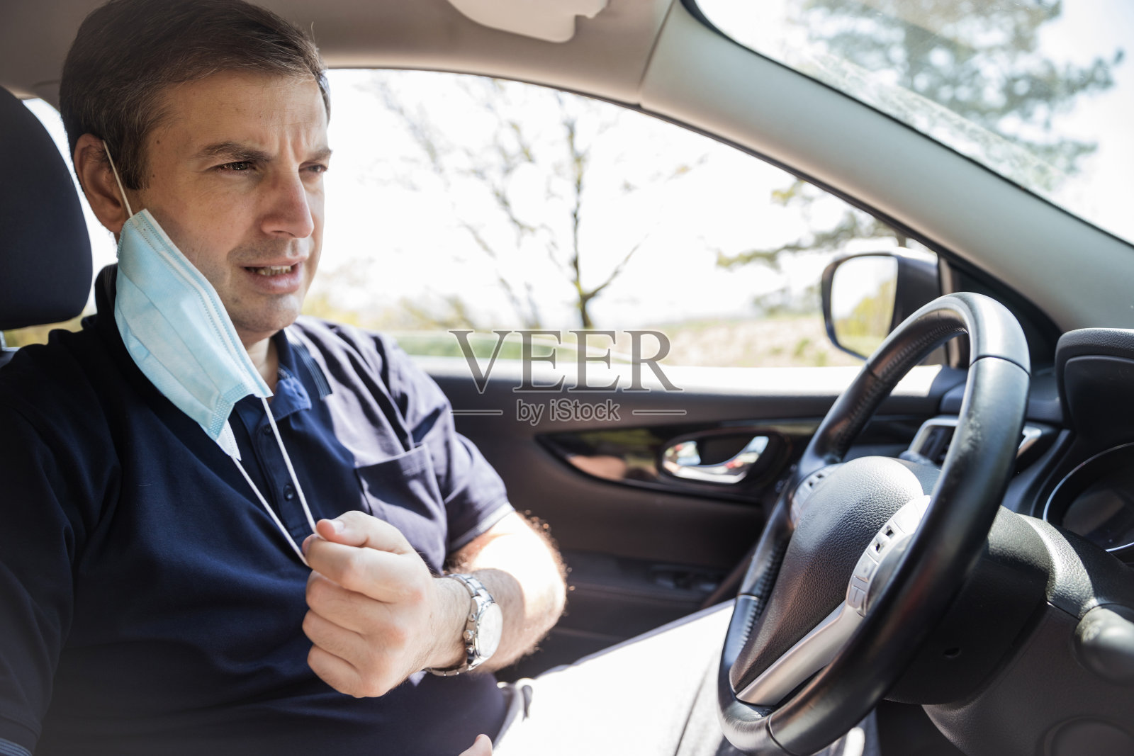 一名男子在车里摘下防护面具,皱着眉头照片摄影图片