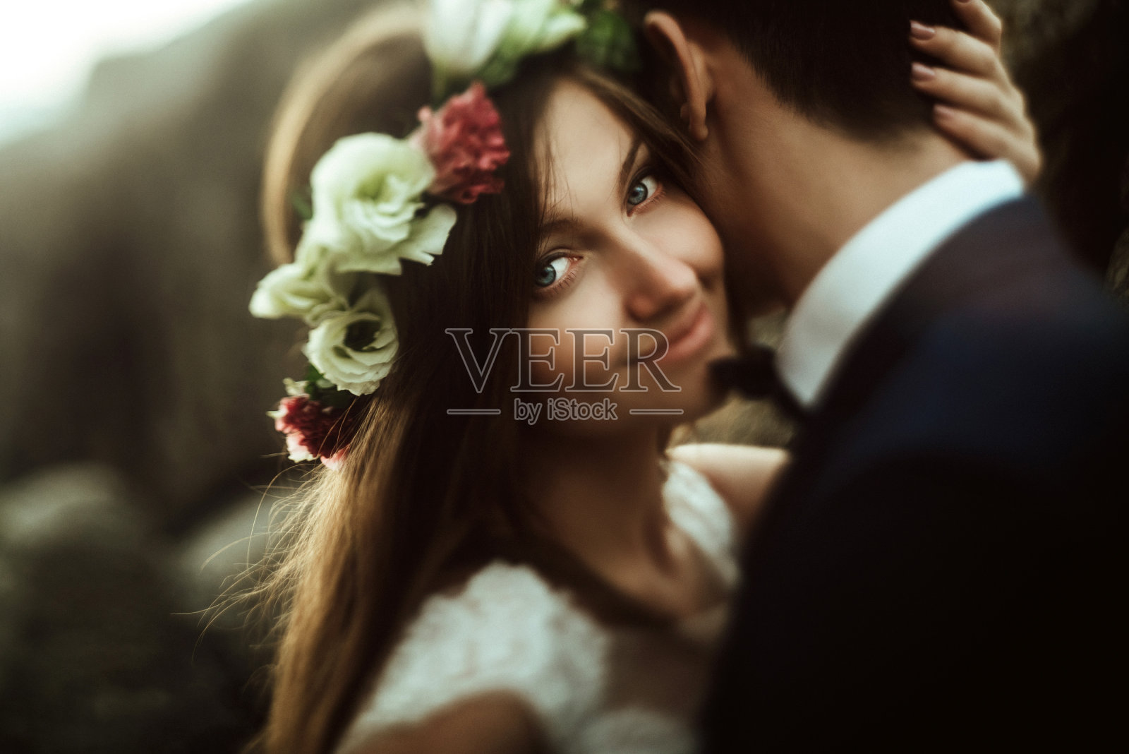 奢华幸福的新娘和时尚的新郎温柔地拥抱在一起,背景是令人惊叹的群山中阳光灿烂的岩石照片摄影图片