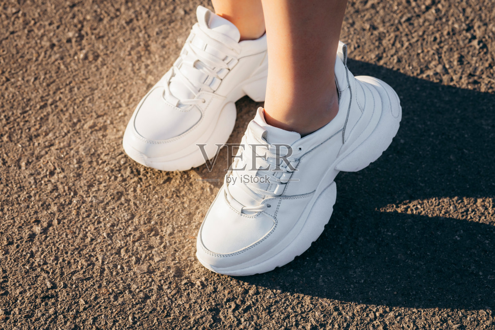 在沥青的背景下,女孩的腿上穿着白色的运动鞋照片摄影图片