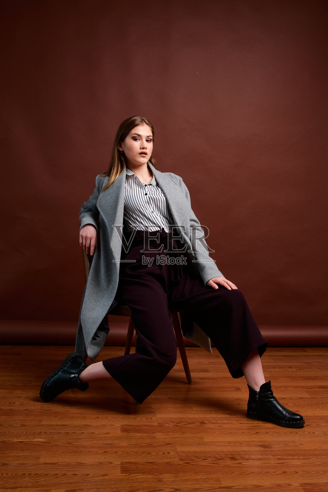 独立的年轻女子在照相馆摆姿势。穿着经典套装和灰色外套的漂亮年轻女性。照片摄影图片