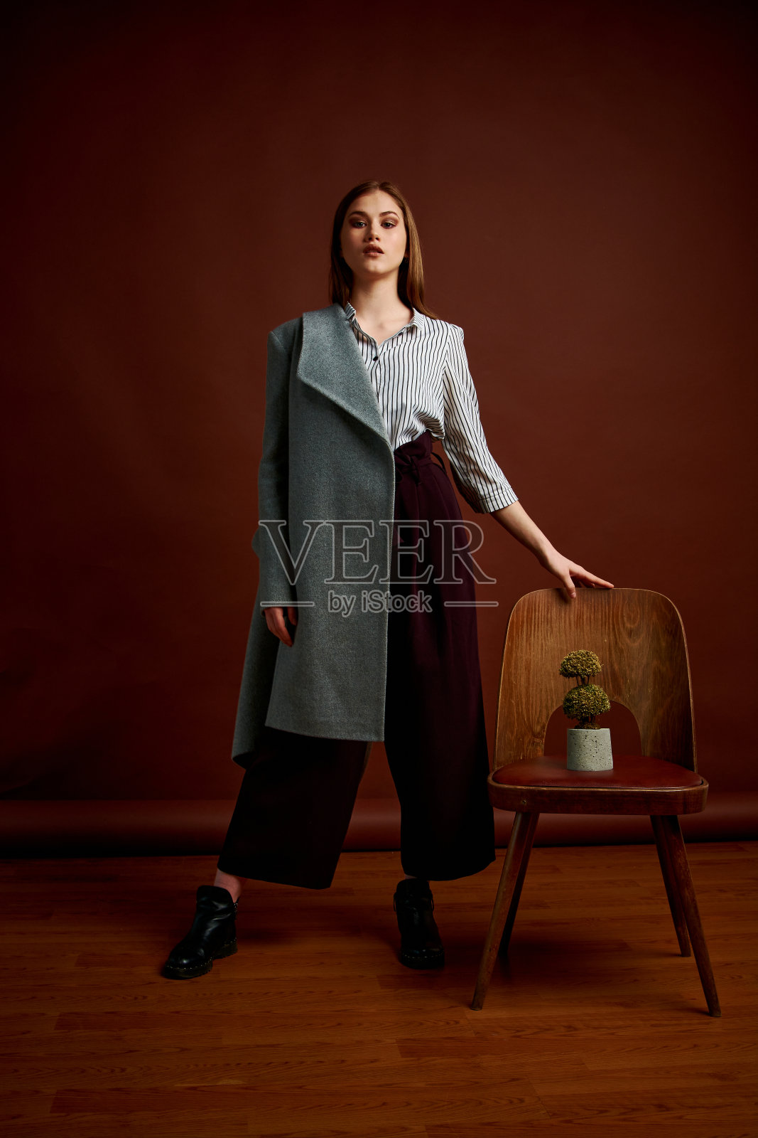 漂亮的年轻女性,穿着经典的套装,黑色的鞋子和灰色的外套。古董椅子。女人的衣服。照片摄影图片