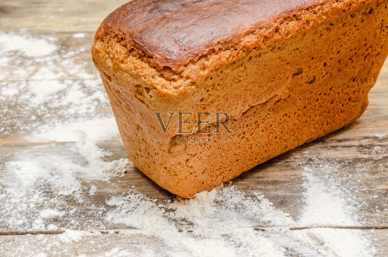 一块面包站在一个木头背景中,面粉分散的特写。本空间照片摄影图片