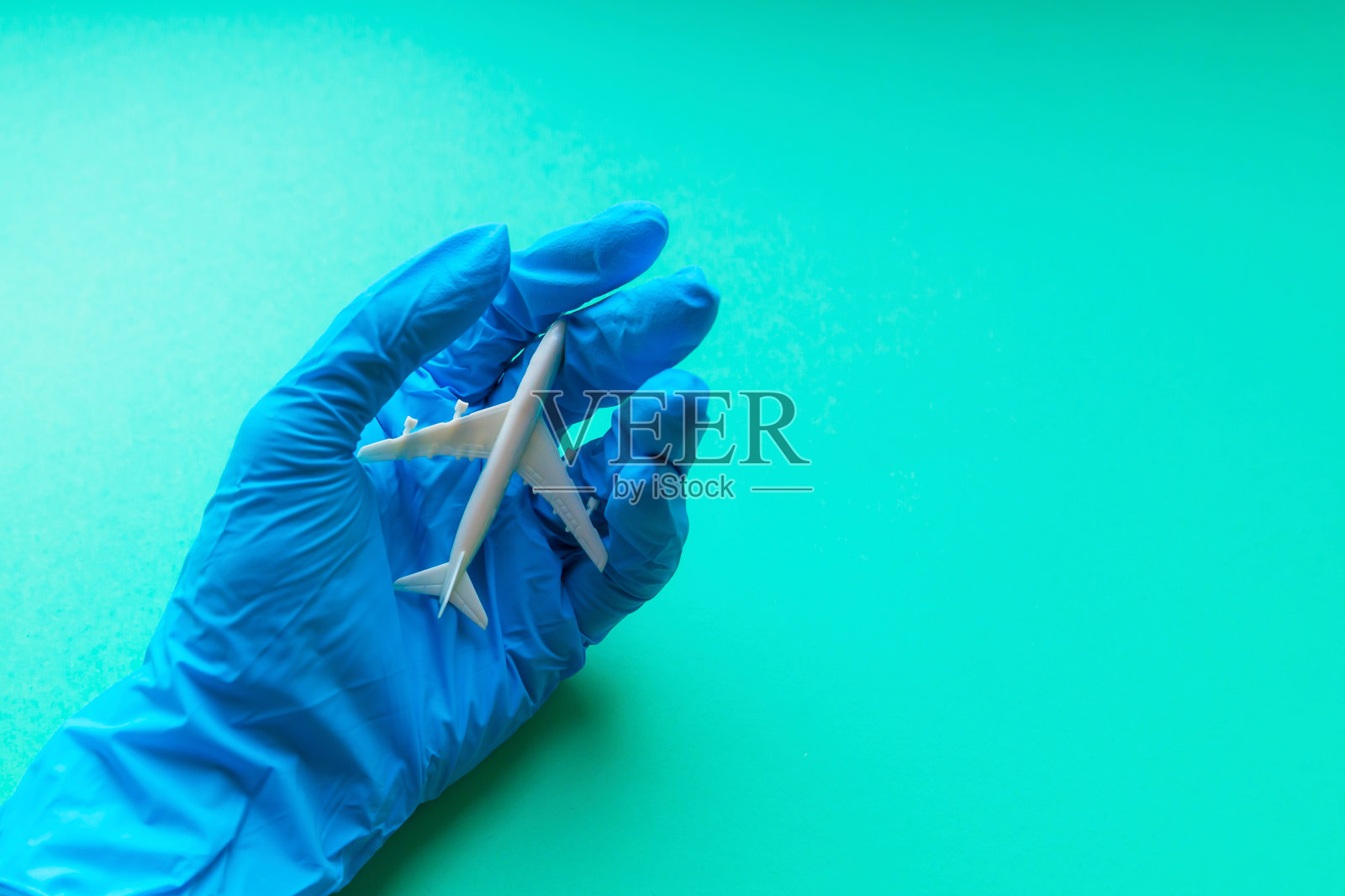 避免不必要的旅行——概念。白色飞机上一只手戴着蓝色防护手套。俯视图,复制空间照片摄影图片