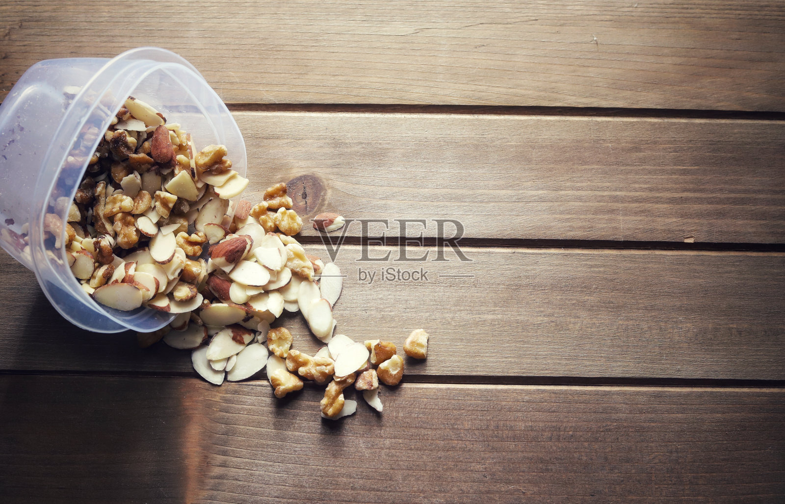 木桌上放着一个装有机杏仁和核桃的塑料容器照片摄影图片