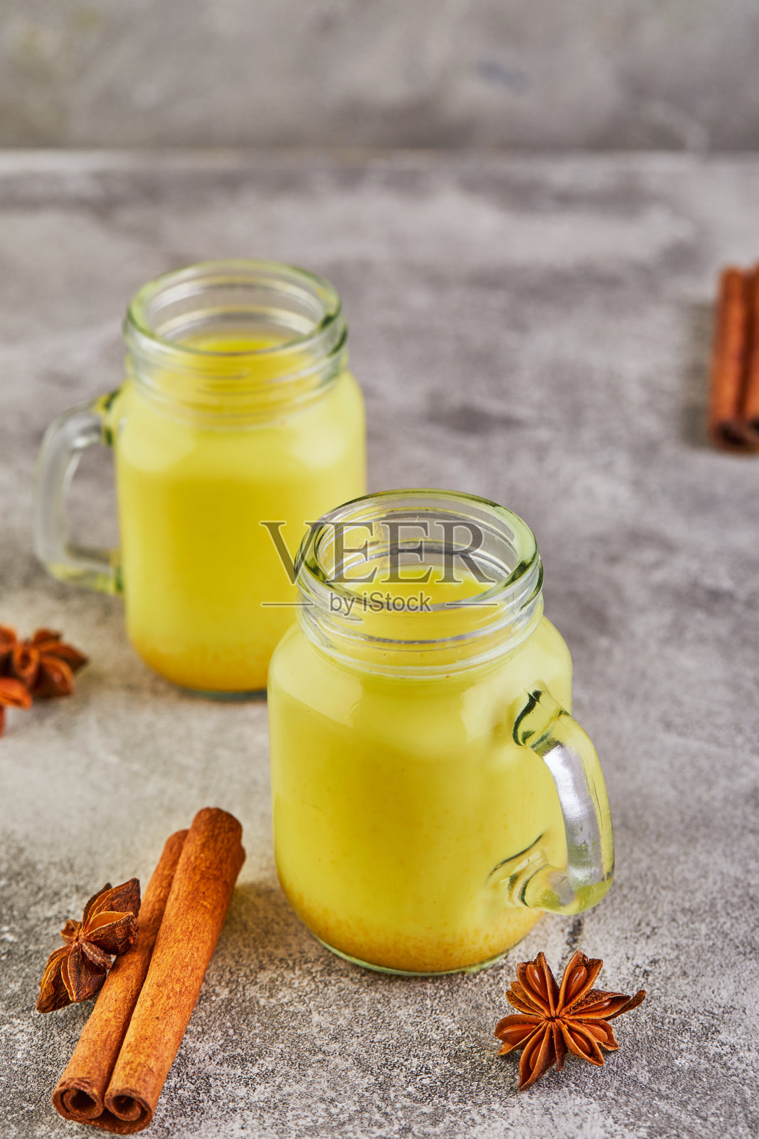 玻璃杯中的金色拿铁姜黄健康饮品,灰色水泥背景上的姜黄牛奶、肉桂棒、姜黄和茴芹,姜黄排毒茶和原料照片摄影图片