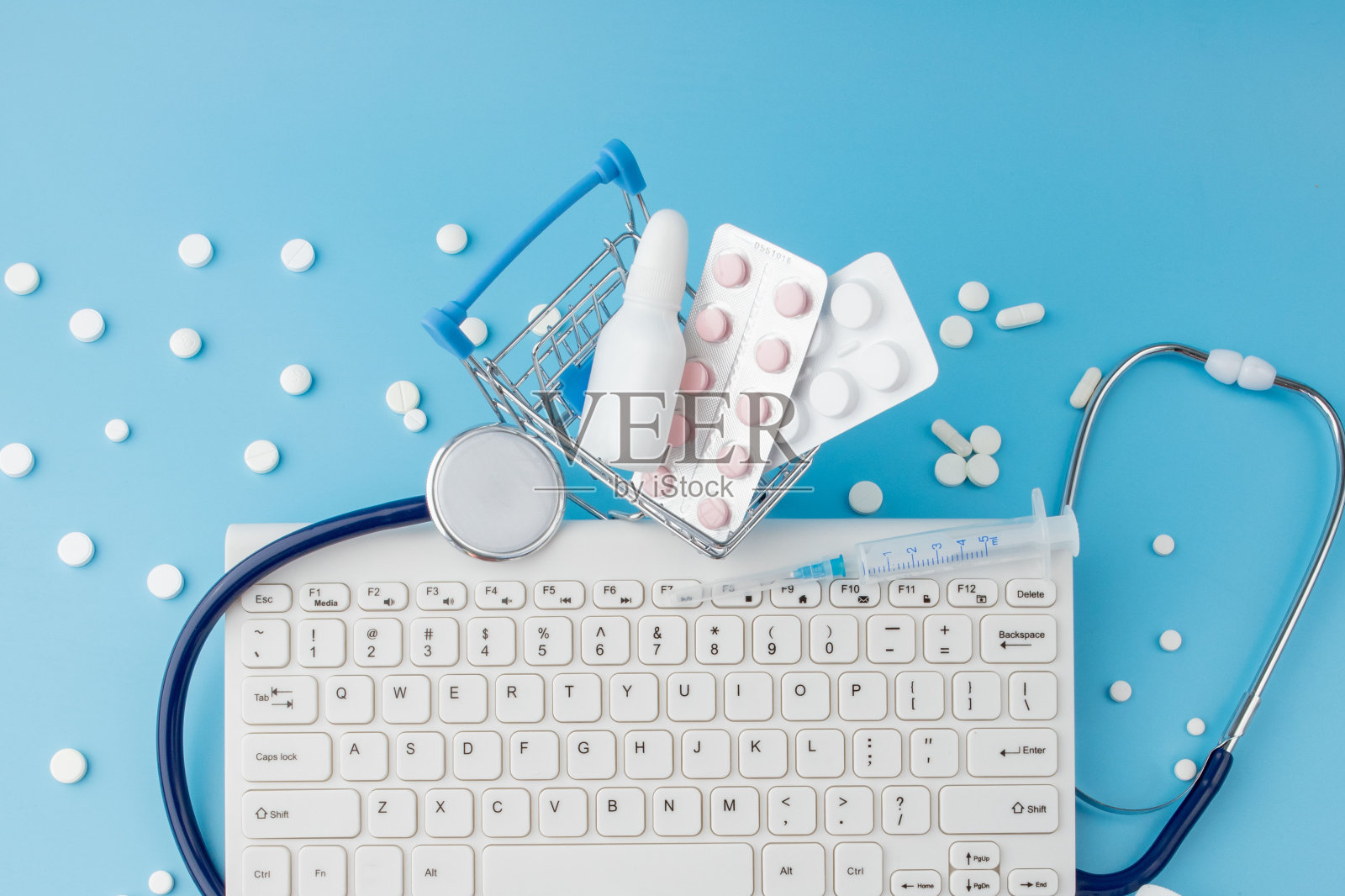 购物车玩具与药物和键盘。药片,吸塑包装,药瓶,温度计,蓝色背景防护面罩…医疗保健和网上购物。顶部视图与地方为您的文本照片摄影图片