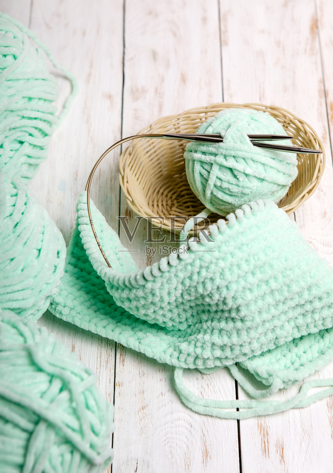 用针织针装在篮子里的纱线团。木制背景上的几束羊毛和编织针照片摄影图片