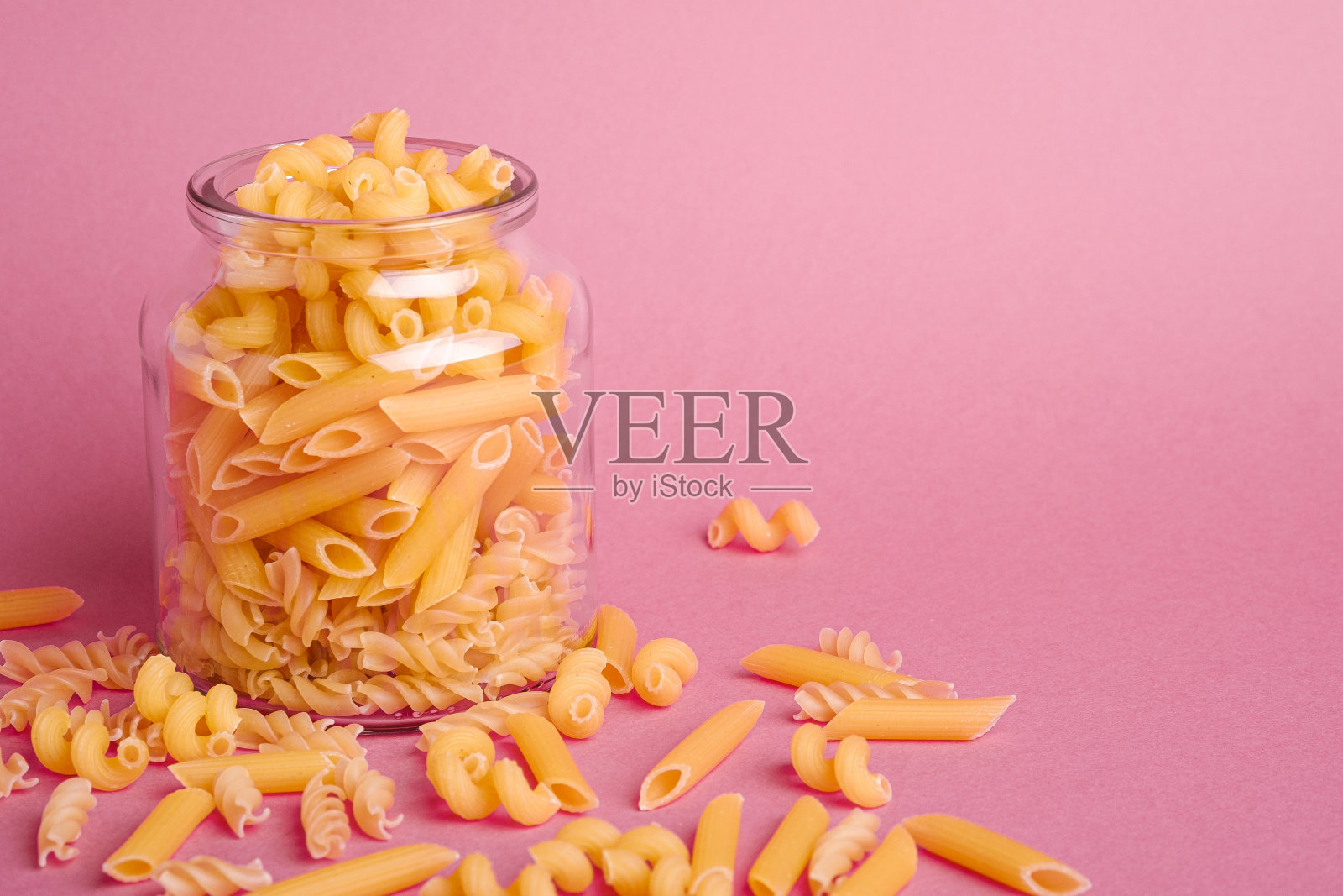 一个玻璃罐与各种生小麦面条在最小的粉红色背景,视角宏观,复制空间照片摄影图片