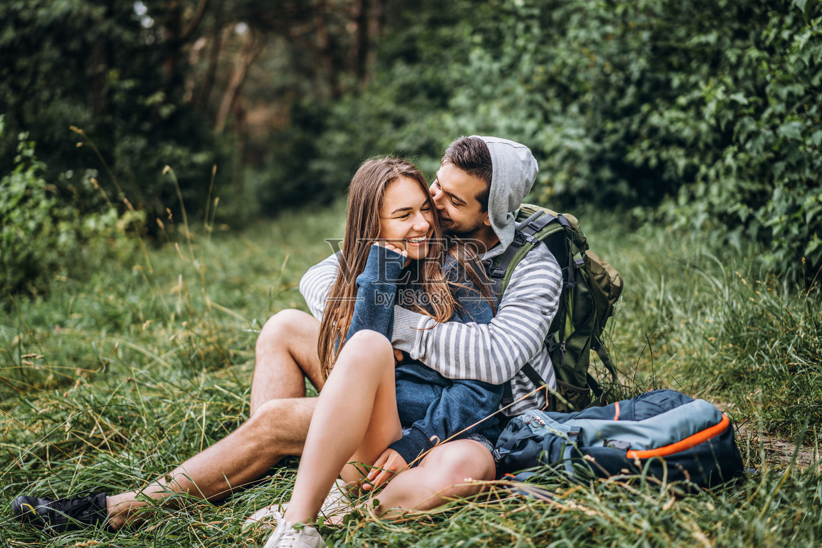 长发女子和背着背包坐在森林草地上的男子。享受大自然的乐趣,拥抱和亲吻照片摄影图片