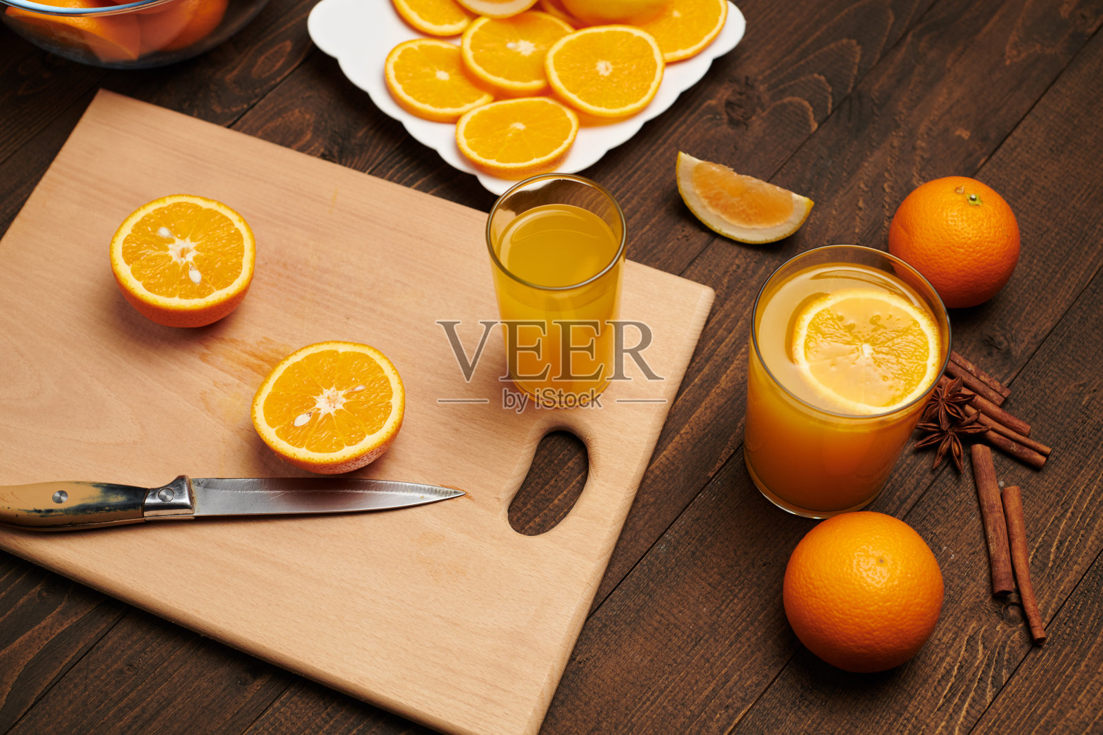 新鲜的橘子切片放在木桌上,切菜板和菜刀上。一盘柑橘片——天然健康的食物。一杯水果鸡尾酒。照片摄影图片